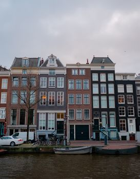 Scenic view of classic Amsterdam rowhouses by a canal with boats and bicycles.
