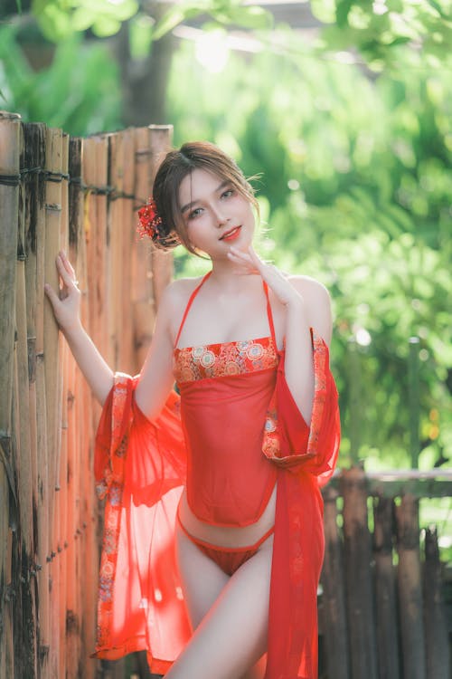 A woman in a red dress posing near a fence