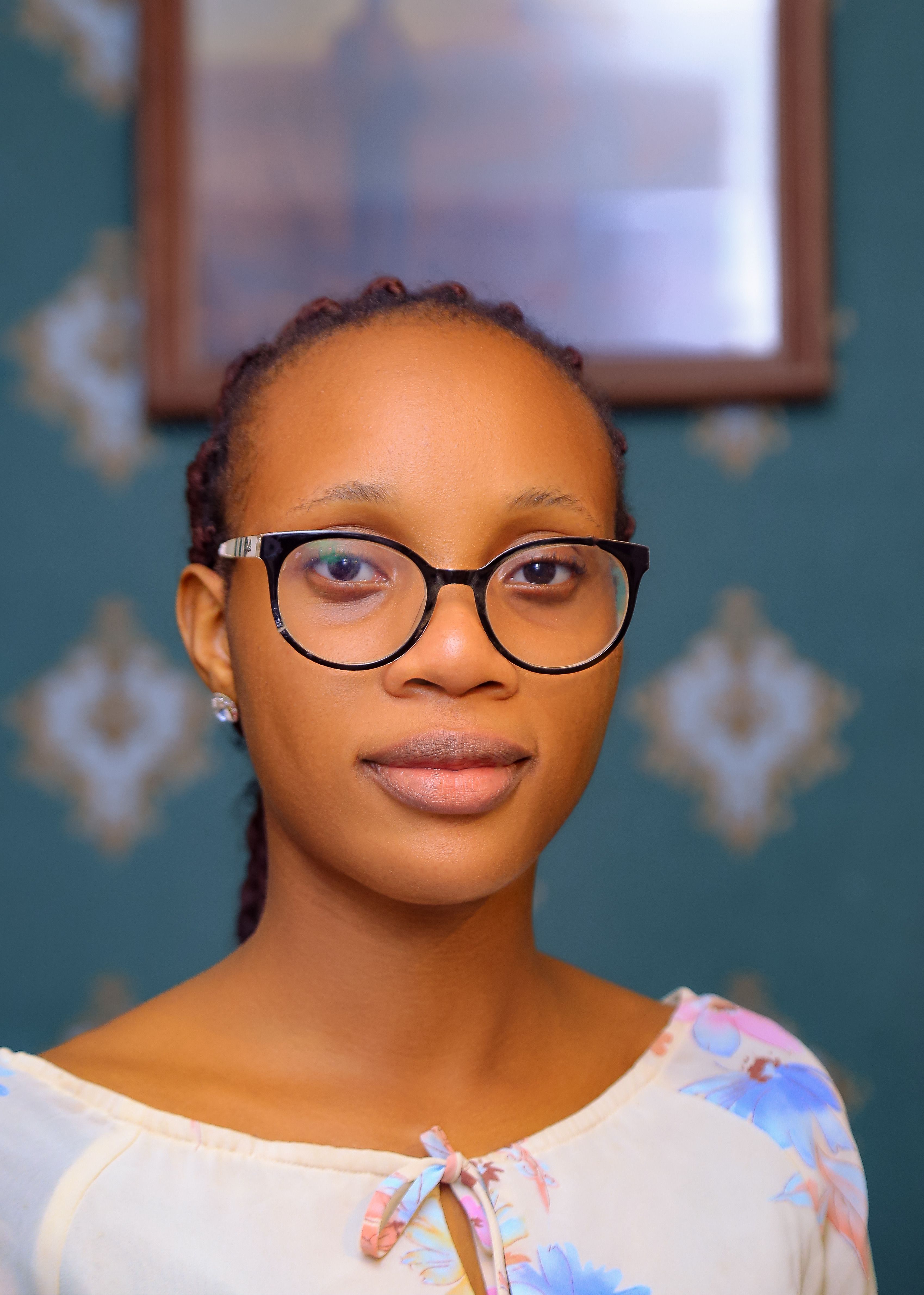 Portrait of a young woman with glasses wearing a floral blouse indoors.