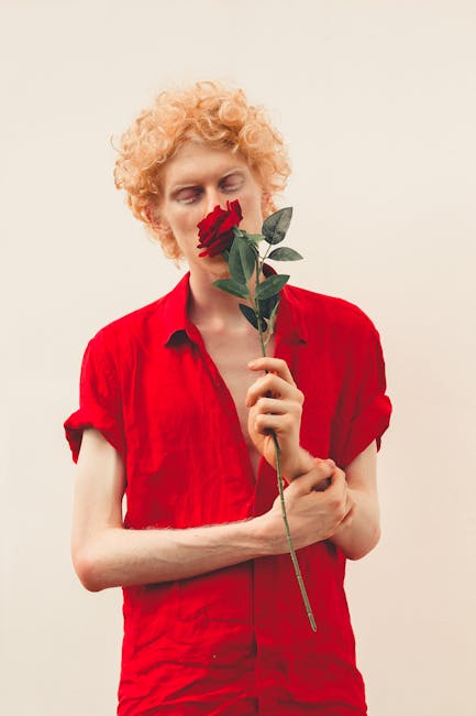 A man in a vibrant red shirt holds a delicate red rose, creating a striking and stylish portrait.