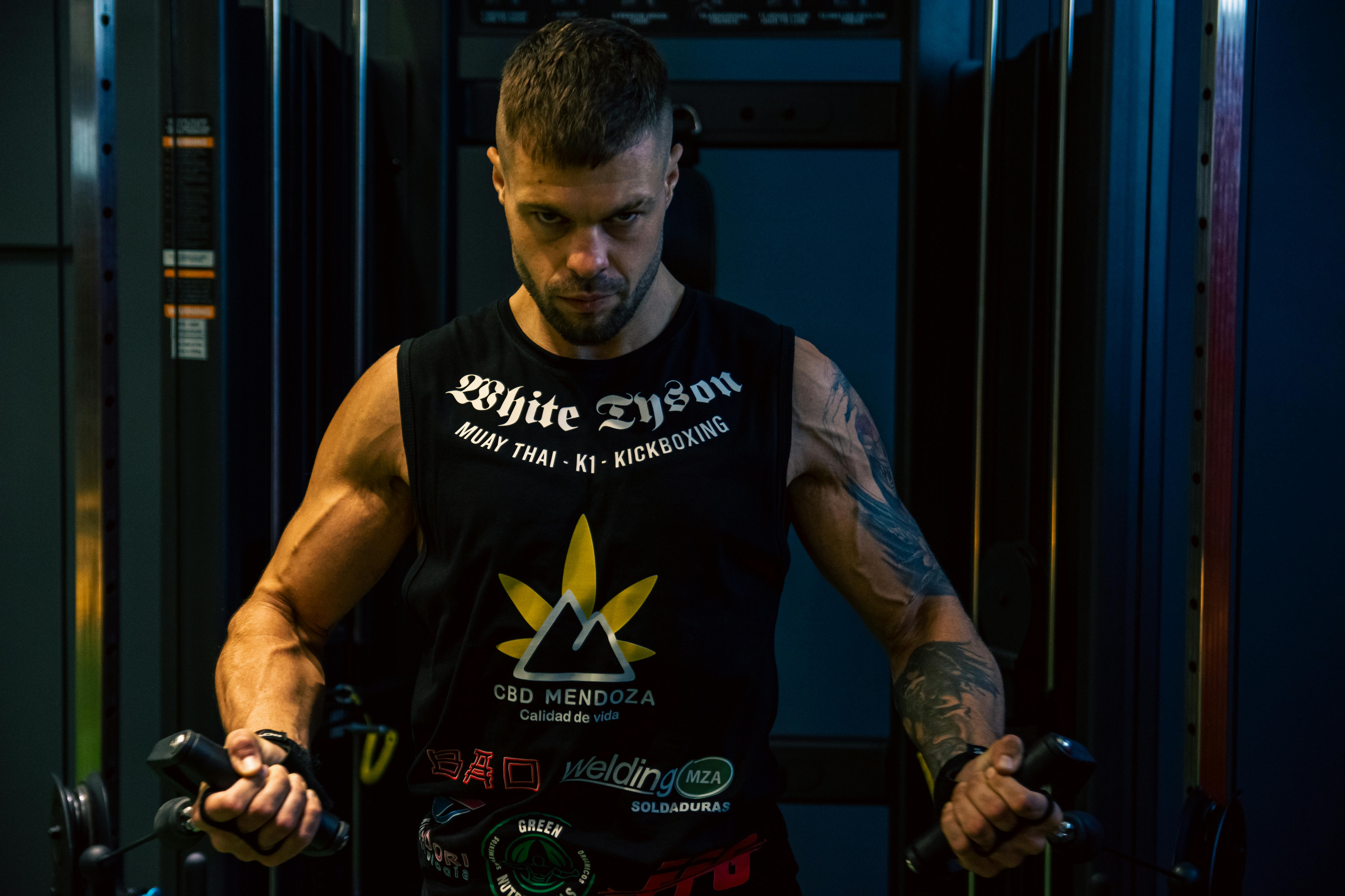 Focused man with tattoos works out in a dimly lit gym, showcasing strength and determination.