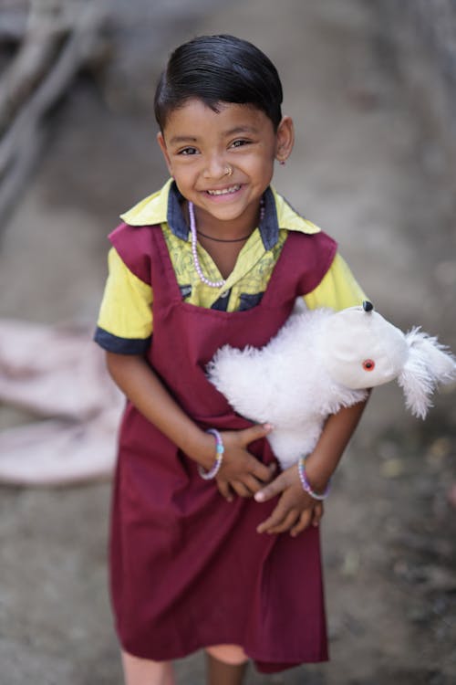 Free A Little Girl in a Dress Holding a Cuddly Toy and Smiling  Stock Photo