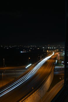 Aerial view of a nighttime city highway with long exposure light trails creating a dynamic visual effect.