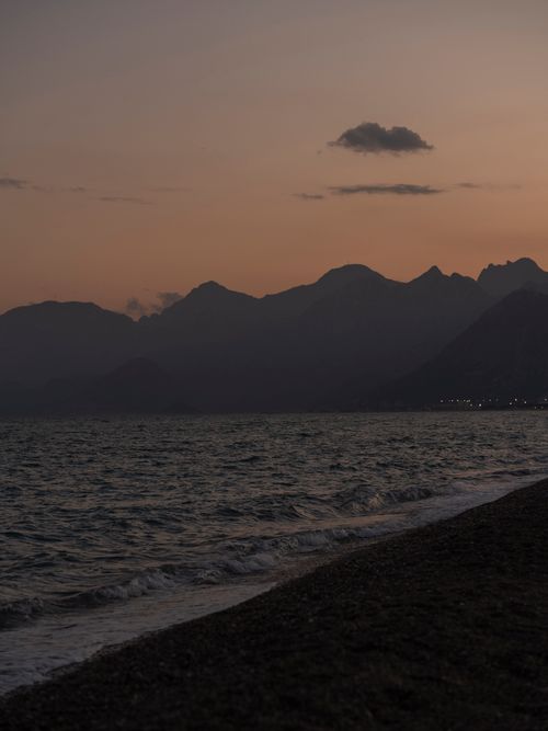 Free A serene beach at sunset with mountains silhouetted against the dusky sky. Stock Photo