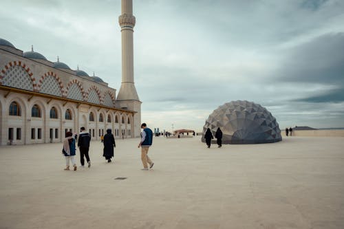 People walk around a large dome in front of a mosque