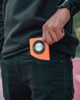 Close-up of a person placing a bright music player into a jeans pocket.