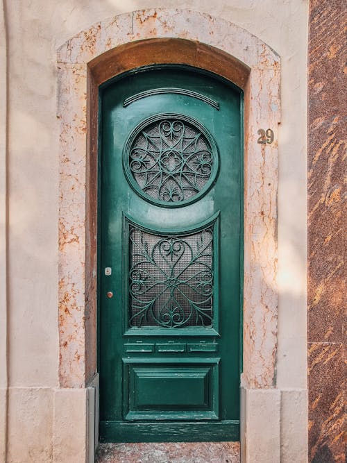 Facade of old house with green wooden door ornate with frosted glass and decorative wrought metalwork patterns. Vintage door found in Portugal