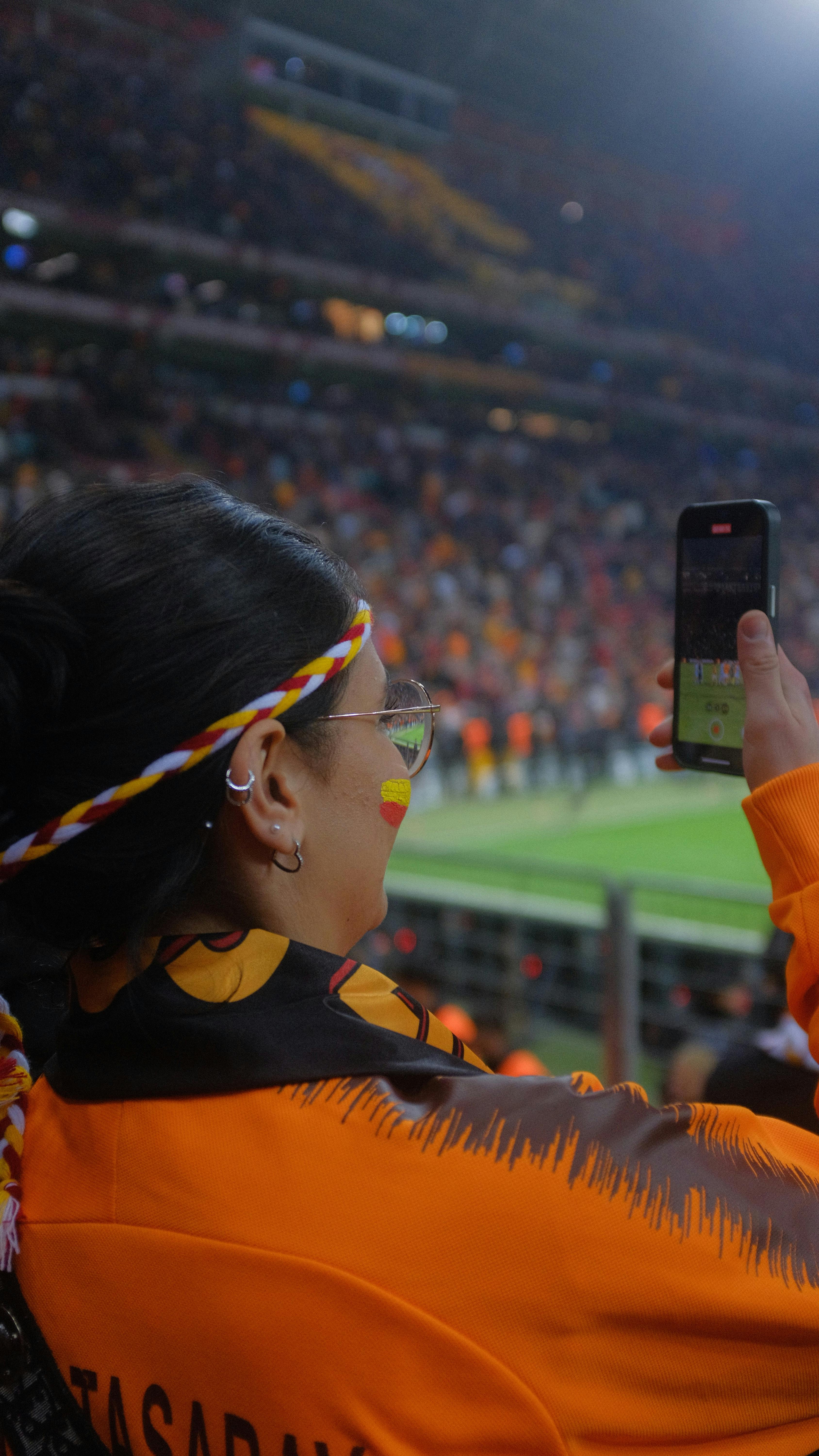 A woman records a live soccer match using her smartphone in a packed stadium.