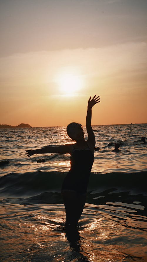 Person Standing with Arm Raised on Sea Shore at Sunset