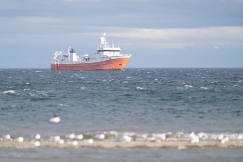 A large orange boat in the ocean near some seagulls