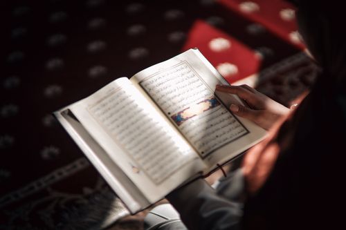 Free Person reading a Quran in a sunlit room, symbolizing spirituality and reflection. Stock Photo