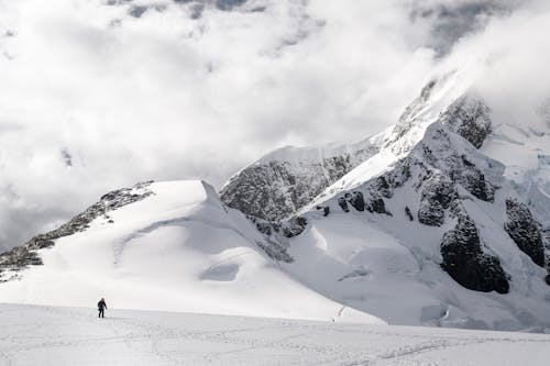 A person walking on a snowy mountain with clouds in the sky