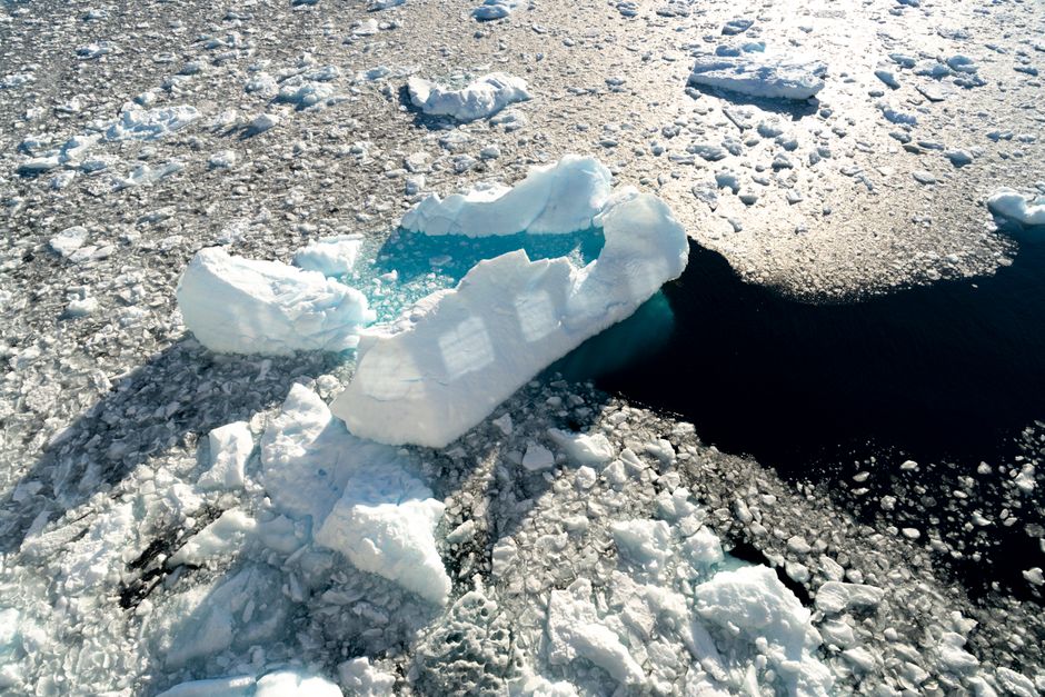 A breathtaking aerial shot of icebergs floating amidst partially frozen waters under sunlight.