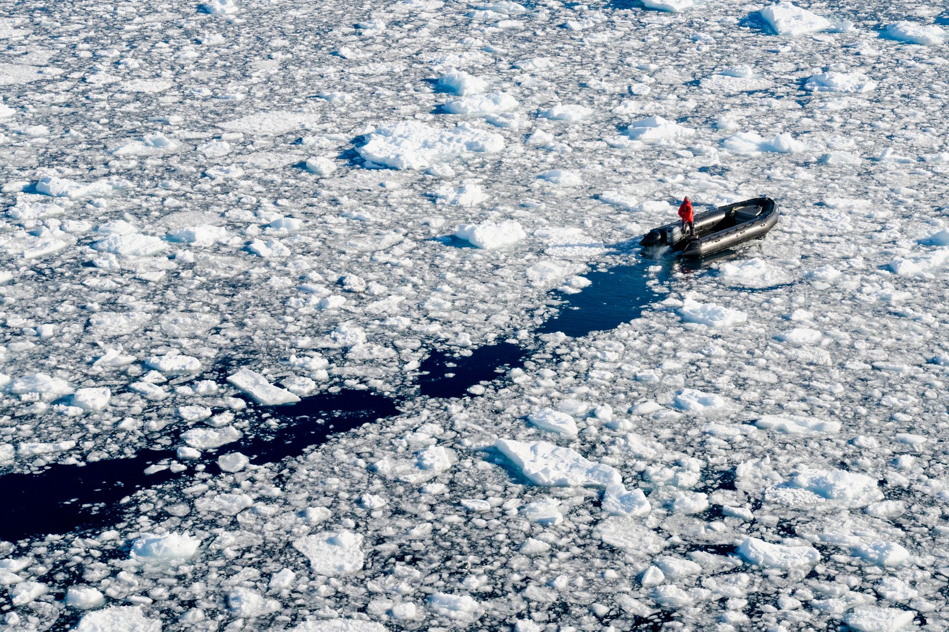 A lone explorer navigates icy waters in a pontoon boat, surrounded by frozen sea ice.