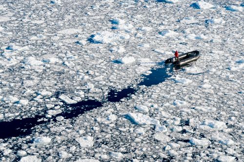 Free A lone explorer navigates icy waters in a pontoon boat, surrounded by frozen sea ice. Stock Photo