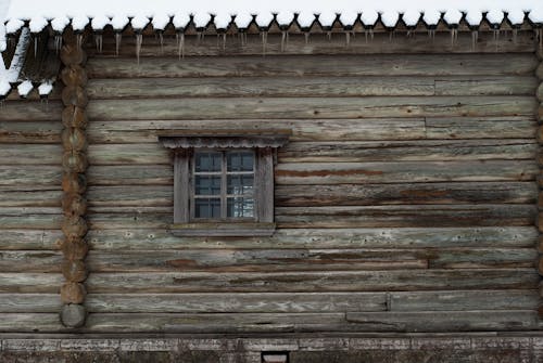 A wooden house with a window and snow on the ground