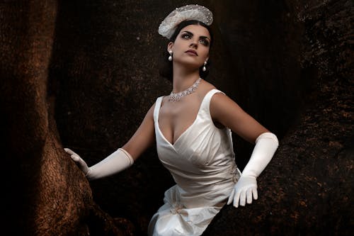 A woman in a white dress and gloves posing in a tree
