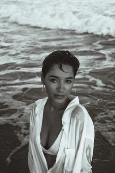 Sultry black and white portrait of a woman at the beach with waves in the background.
