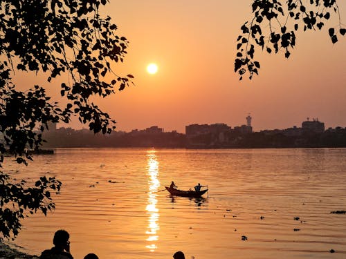 A man is sitting on a boat in the water at sunset