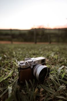 An analogue camera rests on grass during a serene sunset in Itirapina, Brazil.
