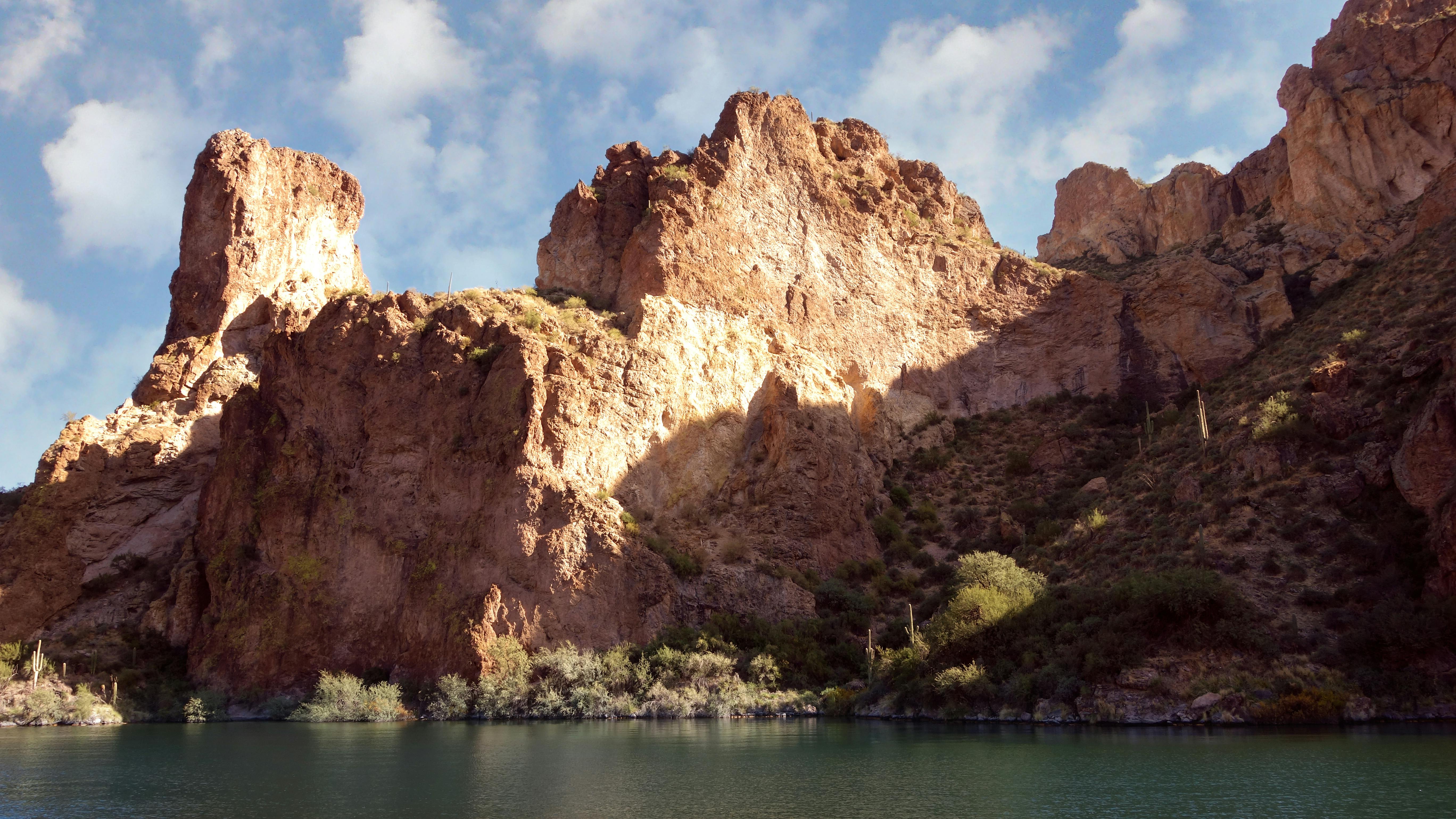 Scenic view of the sunlit cliffs and serene lake in Apache Junction, Arizona.
