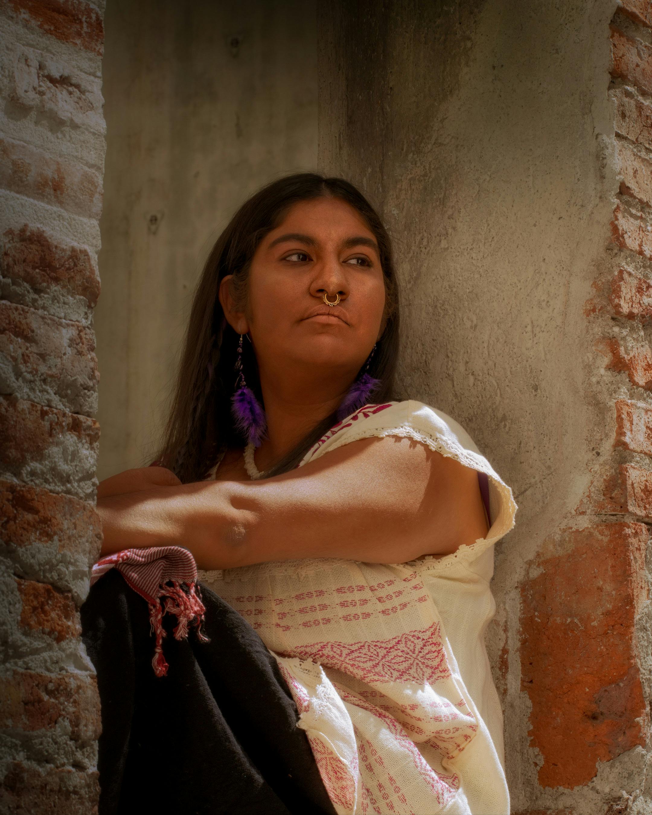 A woman in traditional attire sits thoughtfully against a rustic wall in Ciudad de México, CDMX, México.