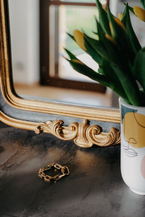 A vase of yellow flowers sits on a table next to a mirror