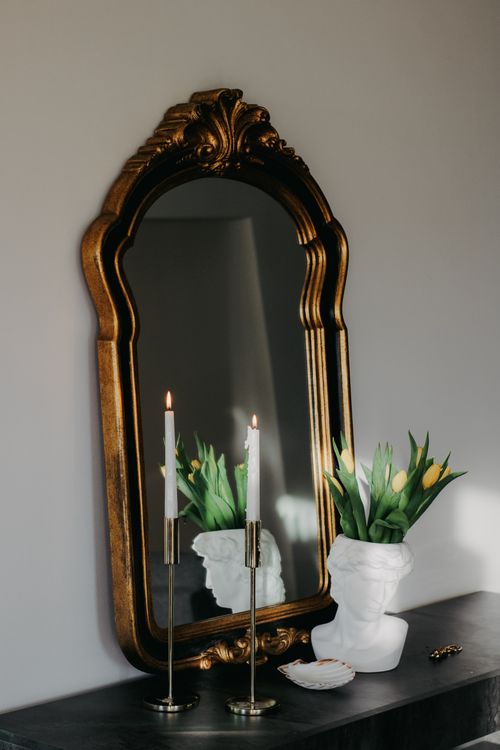 Free Refined interior decor with ornate mirror, candles, and floral bust on a table. Stock Photo