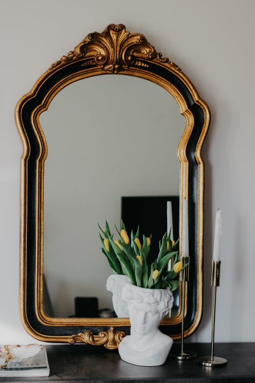 Free A sophisticated interior featuring an ornate mirror, a bust vase with tulips, and elegant candles. Stock Photo