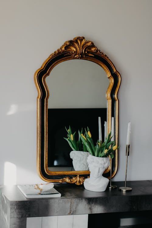 A gold mirror on a black table with a vase