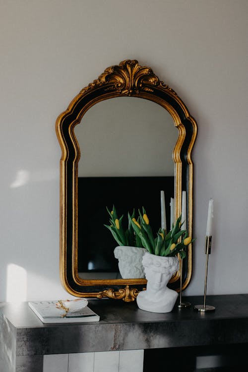 A gold mirror on a black table with a vase of flowers