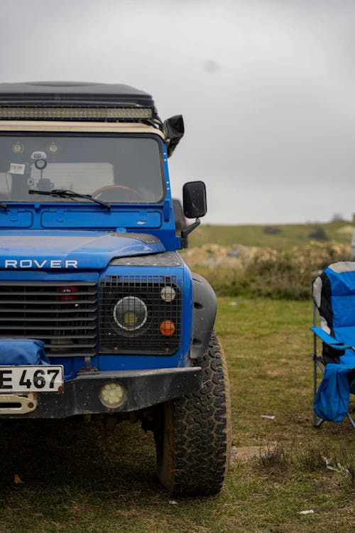 A blue land rover parked in the grass next to a blue tent