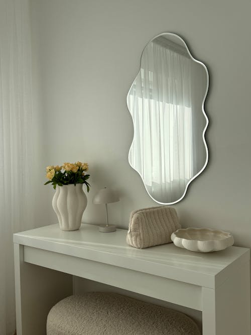 A white vanity with a mirror and a vase
