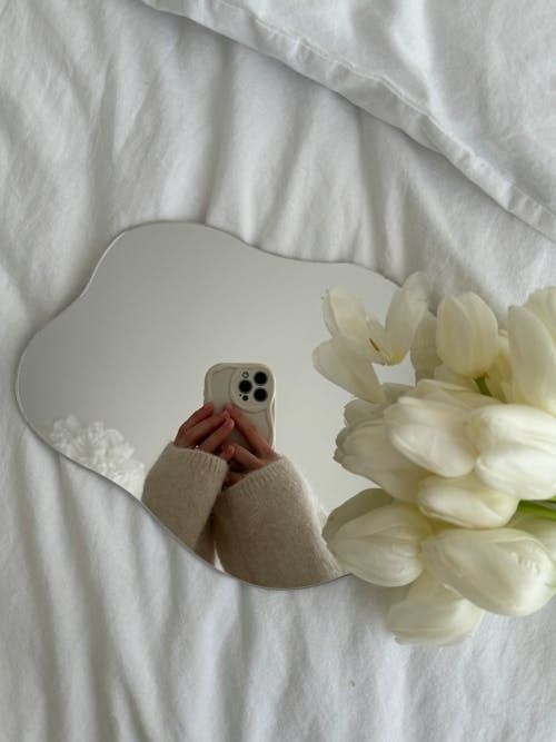 A person taking a picture of a mirror on a bed