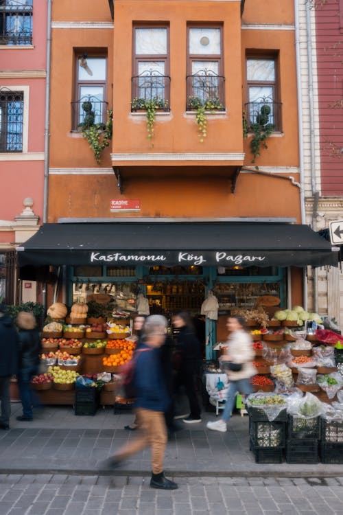 People walking past an open market with fruit and vegetables