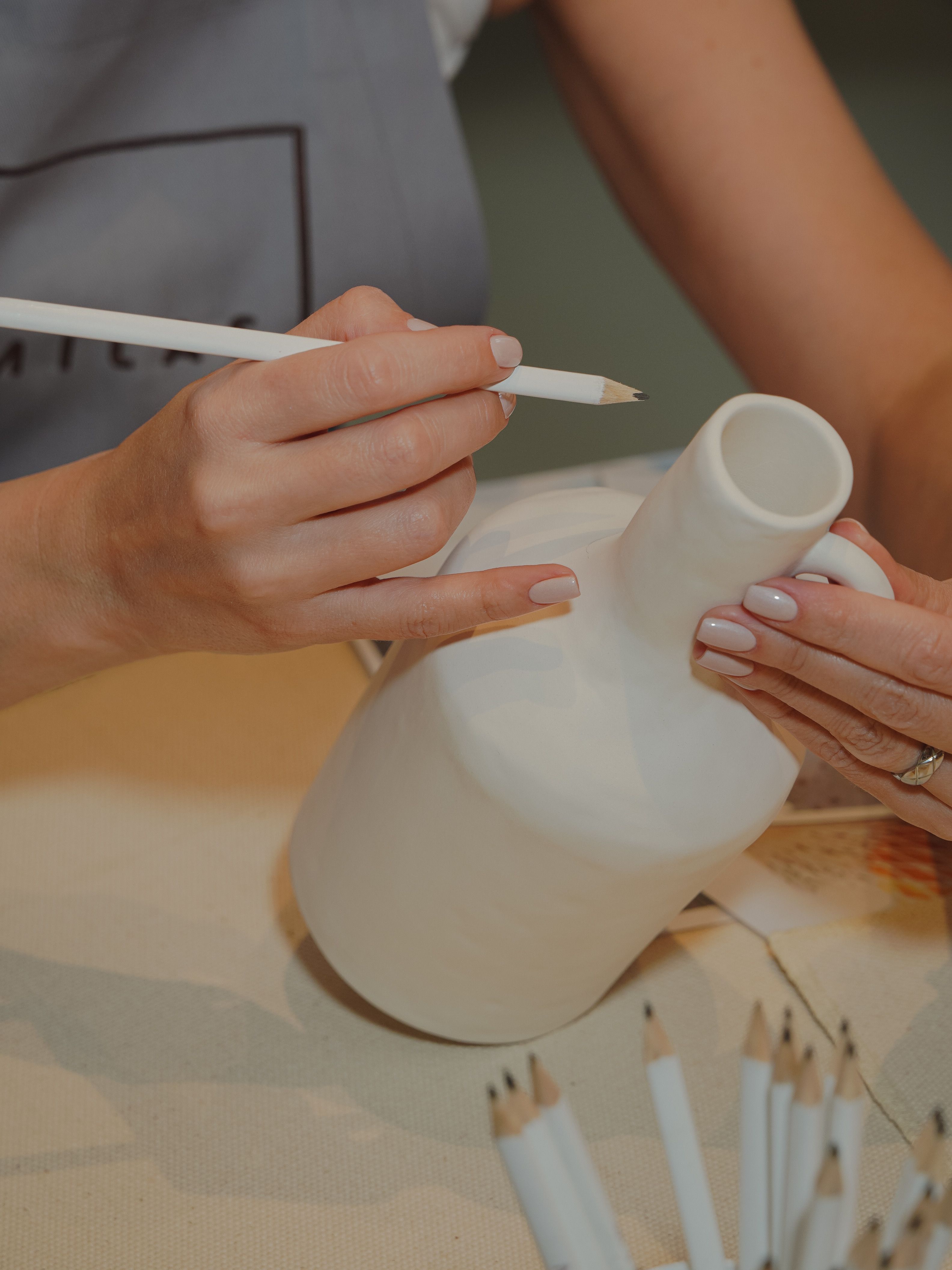 Detailed view of a woman artist drawing on a ceramic vase using a pencil.