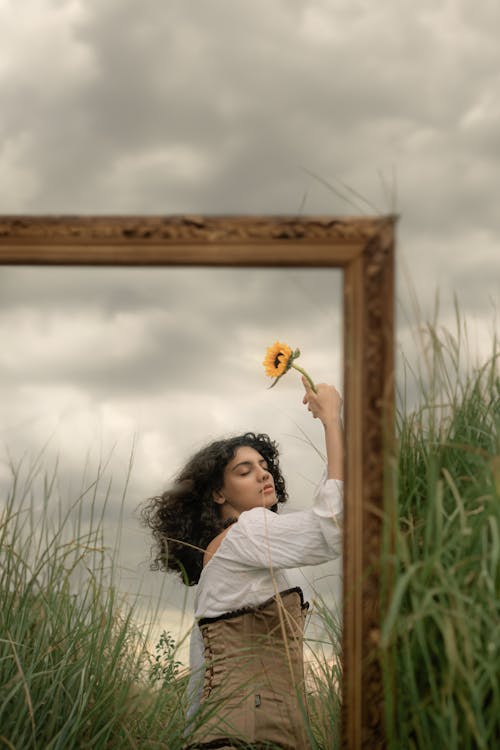 A woman holding a sunflower in front of a mirror