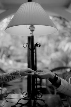 Intimate black and white photo of a couple holding hands under a table lamp, exuding romance and togetherness.