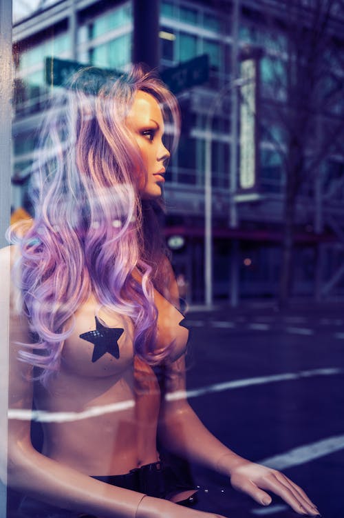 A woman with purple hair and stars on her chest is sitting in a window