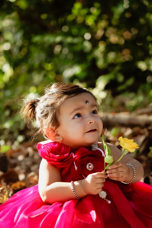 A baby girl in a red dress holding a flower