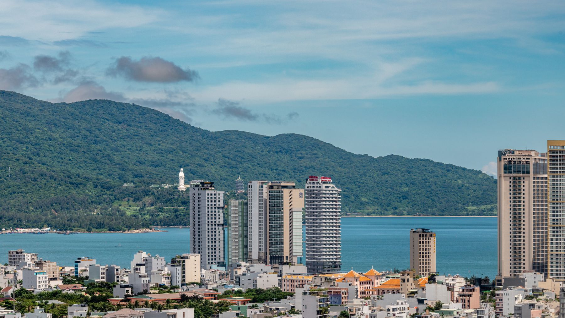 Cityscape of Da Nang, Vietnam with buildings, ocean, and lush mountains.