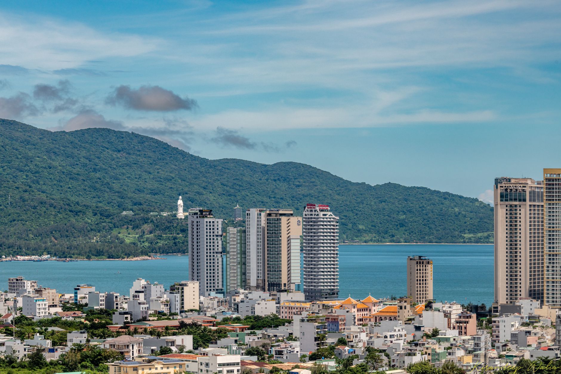 Cityscape of Da Nang, Vietnam with buildings, ocean, and lush mountains.