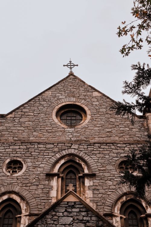 Free Low angle shot of a Gothic church facade with a cross, showcasing intricate stone architecture. Stock Photo