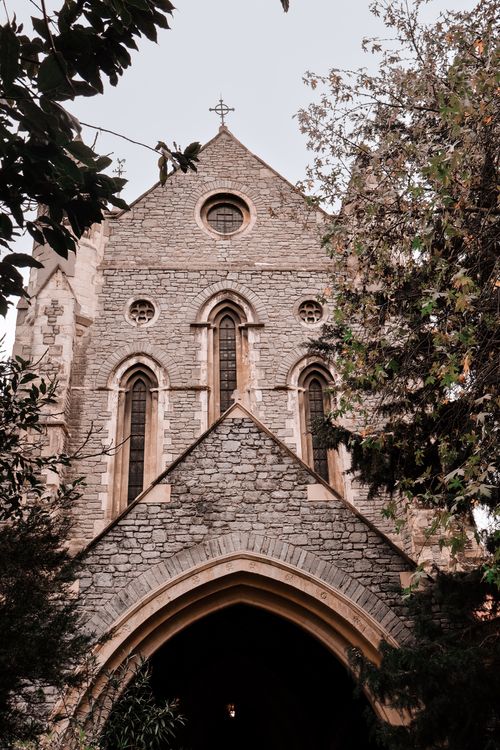 Free Vertical shot of a gothic stone church facade, framed by lush greenery in an urban setting. Stock Photo