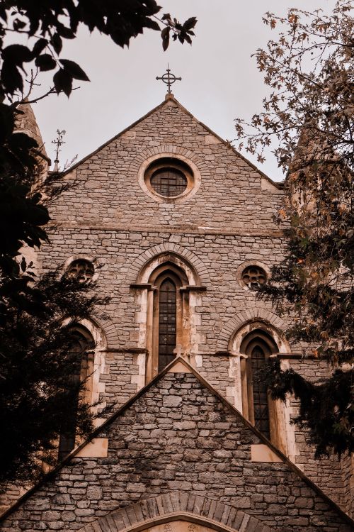 Free A serene view of an old stone church showcasing Gothic architecture surrounded by nature. Stock Photo