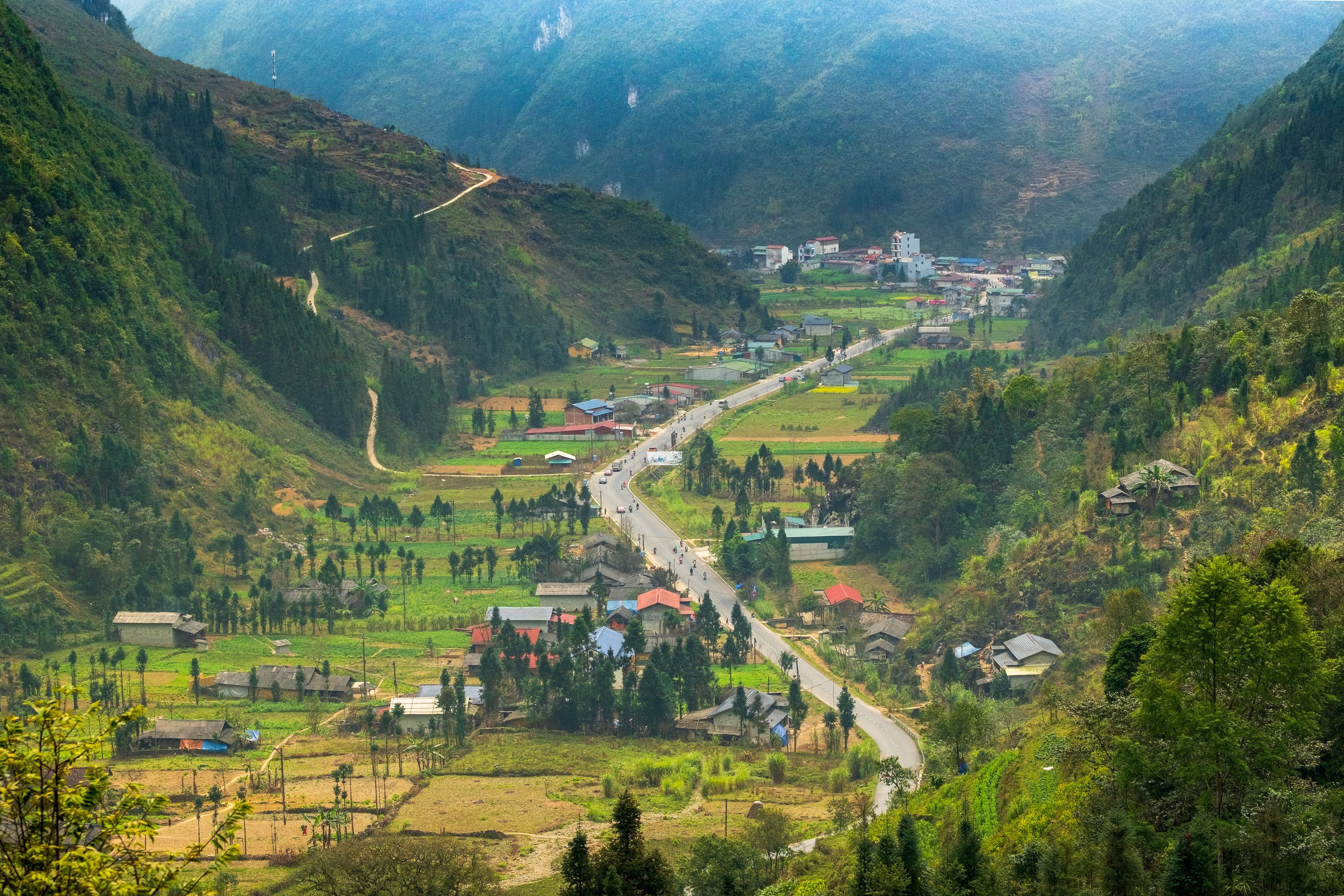 Explore the tranquil mountain valley with lush greenery and a winding road in Hà Giang, Vietnam.