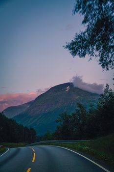A serene twilight view of a winding highway leading to a majestic mountain.