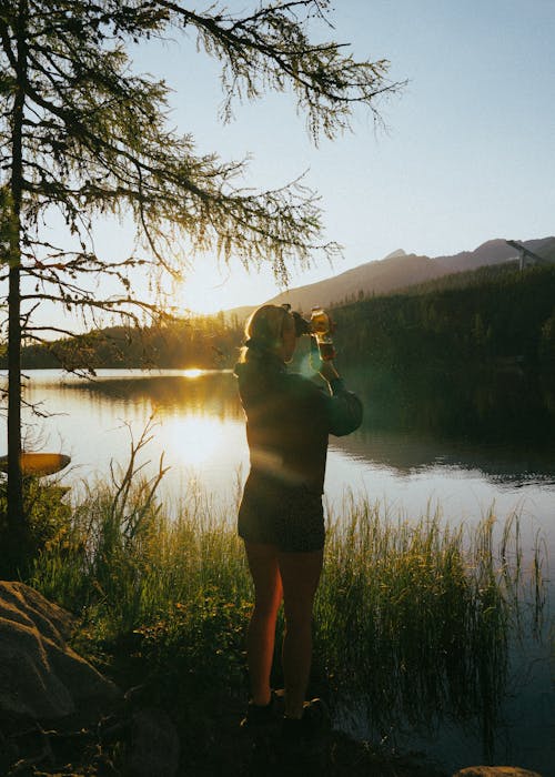 A woman taking a photo of the sun setting over a lake