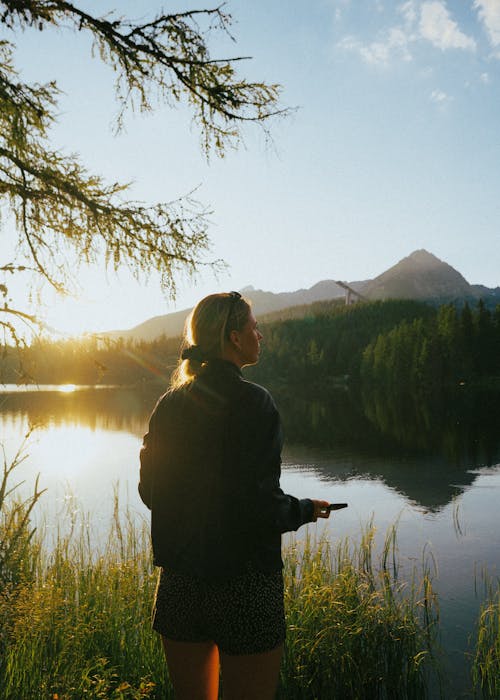 Free A woman standing by a lake with a cell phone Stock Photo