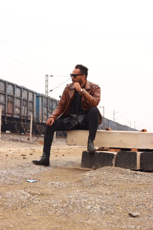 Free A fashionable man in a leather jacket poses by train tracks, exuding a modern urban vibe. Stock Photo